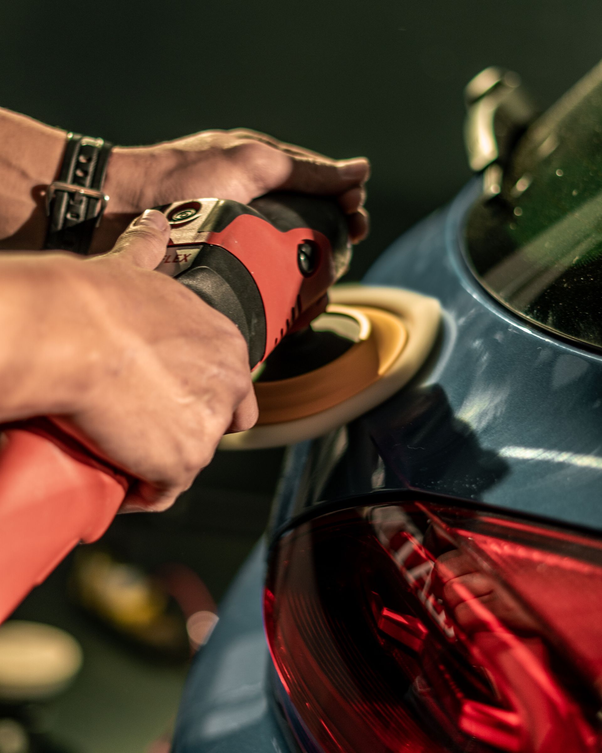 Hand polishing a blue car panel with a rotary tool — paint correction stage at Apex Auto Detailing.