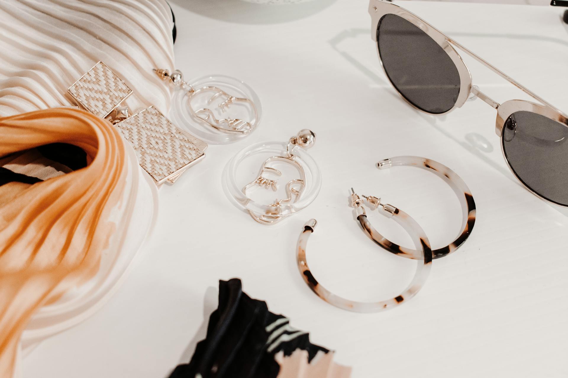 Editorial accessories detail — earrings, sunglasses, scarves on a clean white surface.